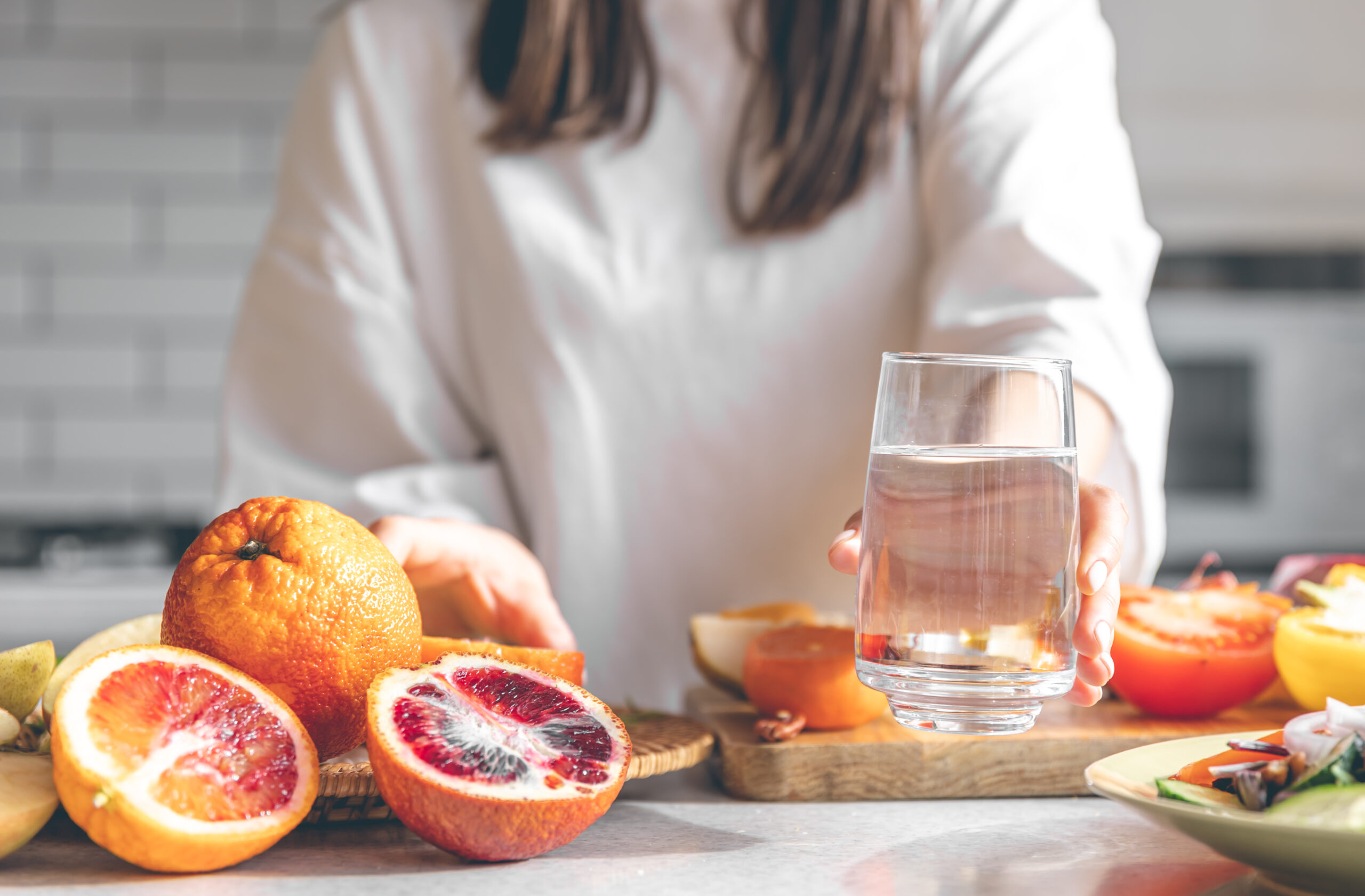 Close-up of a woman’s hands holding a glass of water in the kitchen, symbolizing mindful hydration for nutritional wellness.