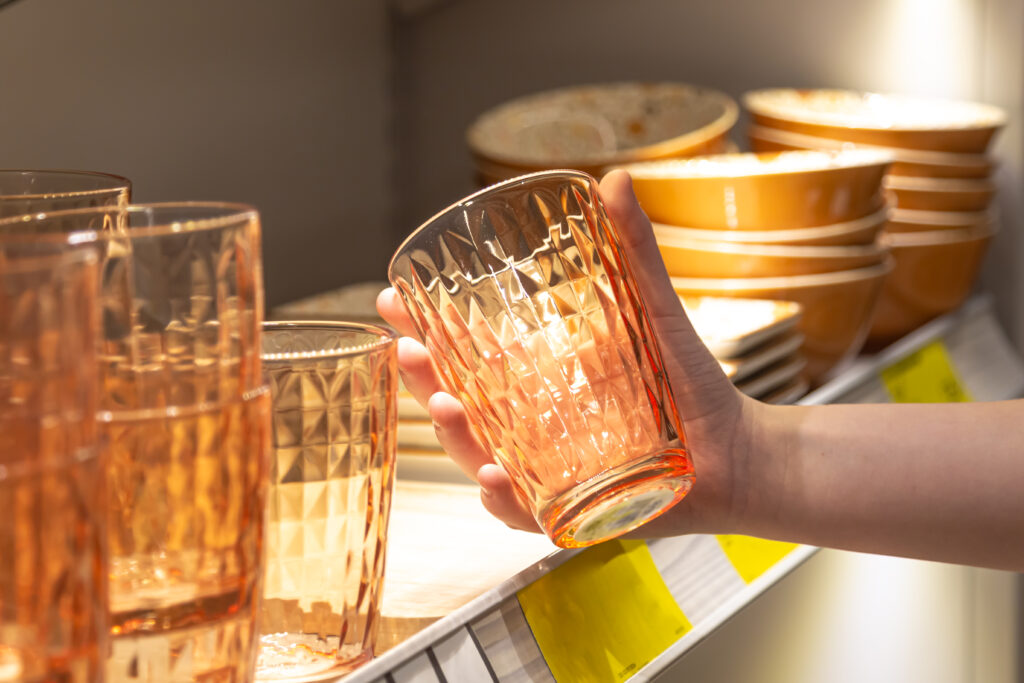 Woman holding a glass from a shelf in a homeware store, representing everyday drinking glasses for cocktails and mindful drinking habits.